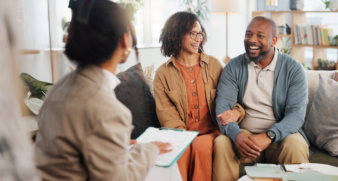 A financial advisor sits with a mature couple on a sofa, reviewing documents related to estate planning, life insurance, and retirement investments.